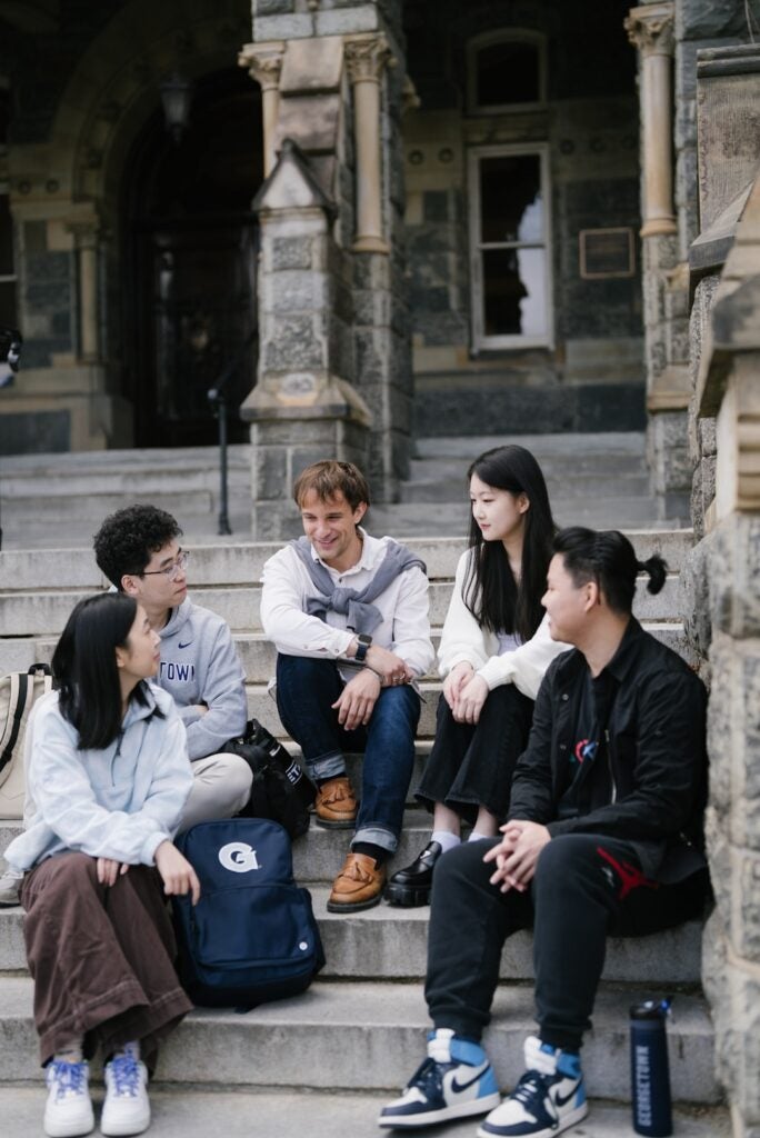 Five Math and Stats students sitting on the steps outside of Healy Hall talking.